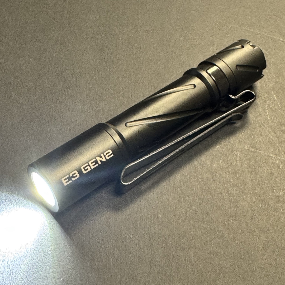 Black Powertac E3 GEN2 AAA flashlight turned on, angled view showing the TIR optic and pocket clip